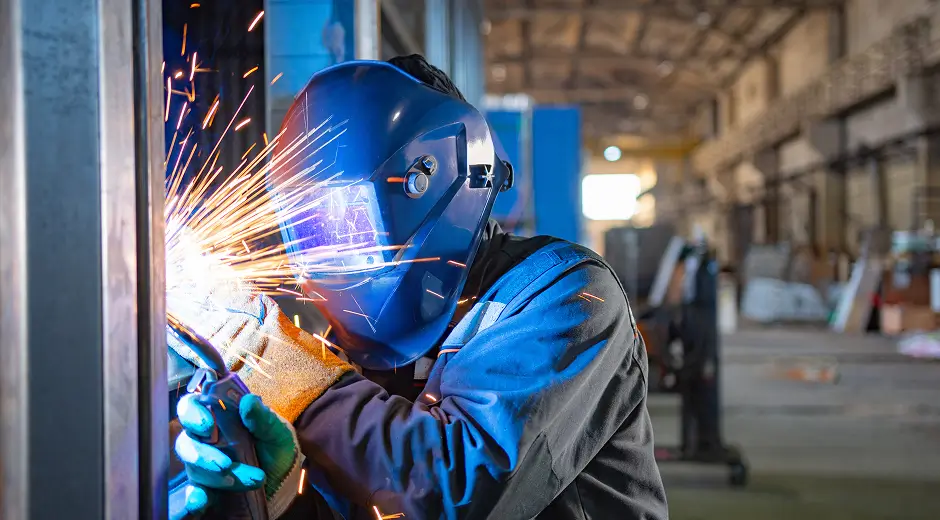 Welder fabricating steel components with sparks flying in an industrial shop