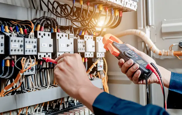 Electrician using a clamp meter to test wiring on an industrial control panel