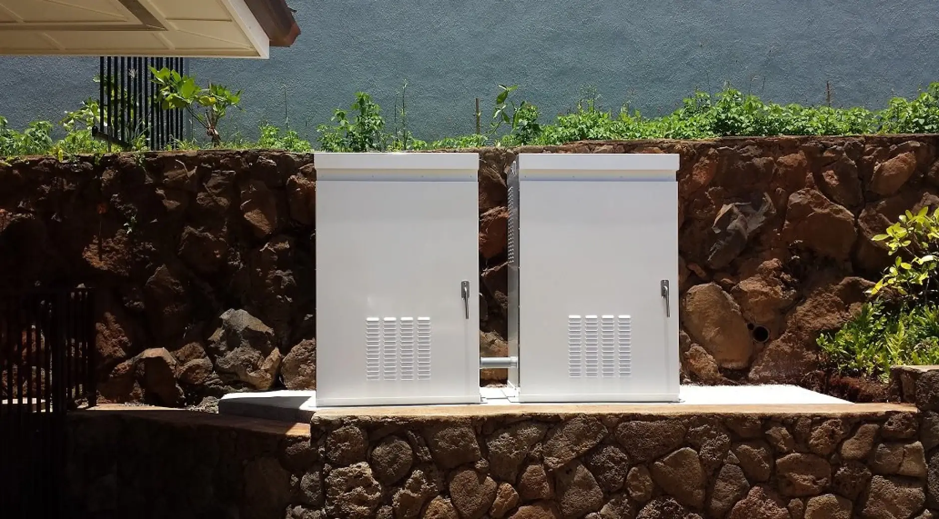 Two white metal outdoor electrical enclosures are pad-mounted on a concrete slab in a coastal outdoor environment