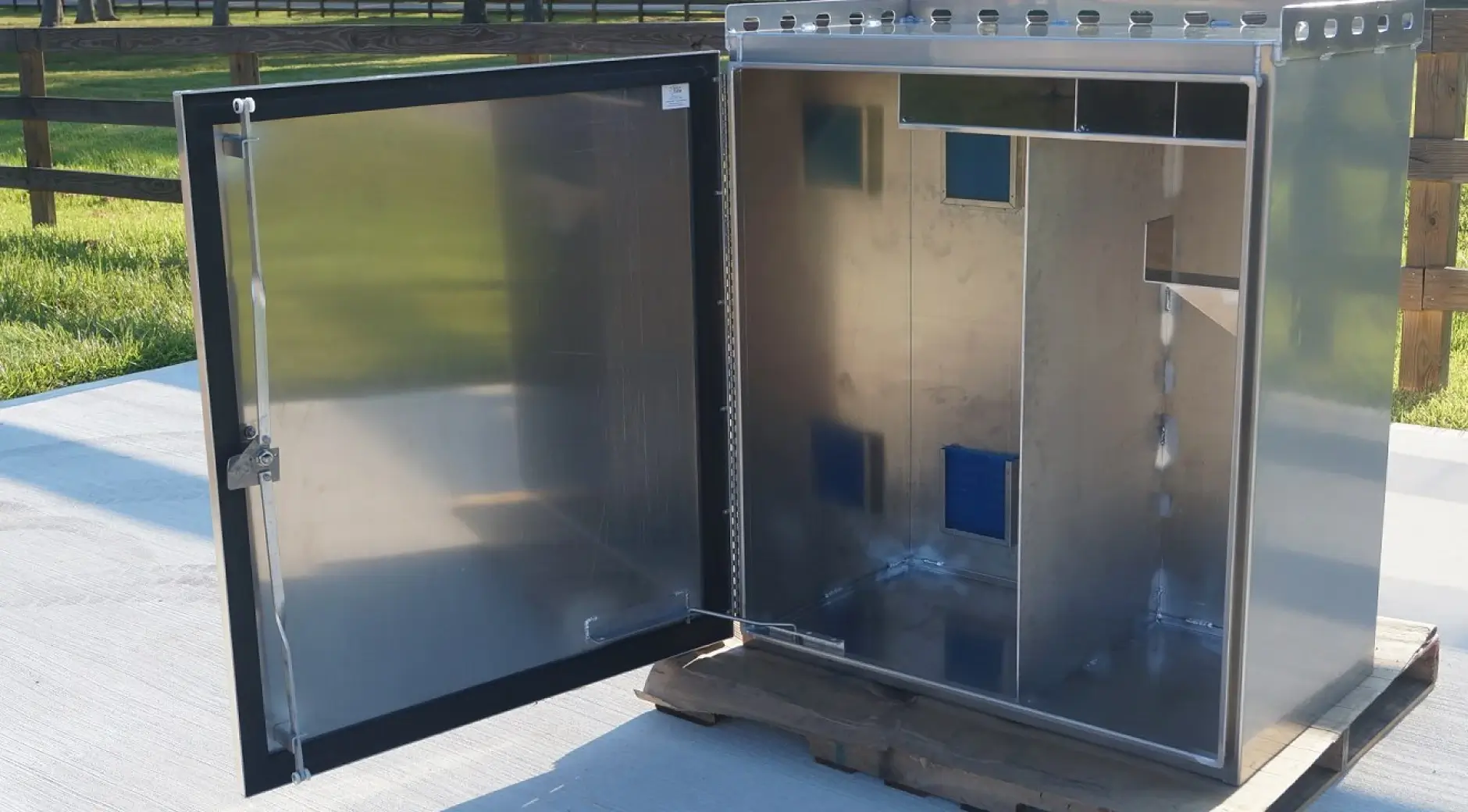 Large stainless steel outdoor electrical enclosure with open door showing interior panel cutouts and weatherproof gasket seal